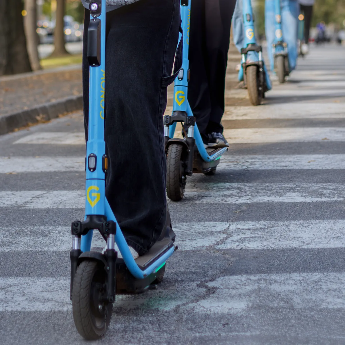 Three riders on GONOW e-scooters crossing a zebra crossing in single file